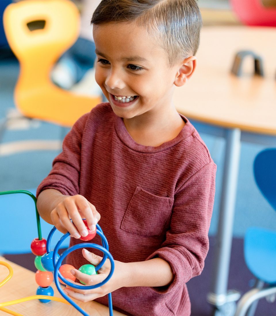 In his daycare classroom, the young boy works independently on a bead puzzle.